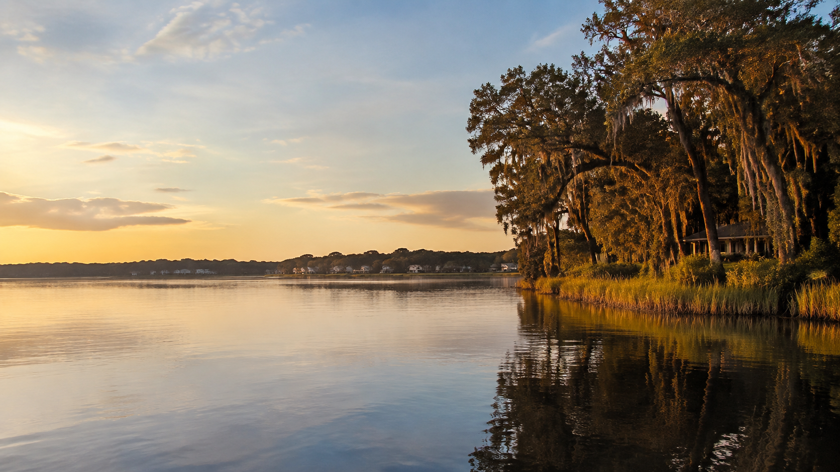 Golden-hour view across the calm St. Johns River, with moss-draped live oaks along the shoreline.